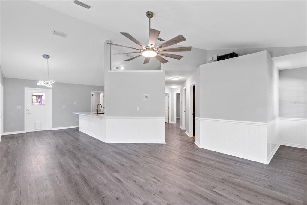 An open-concept living area features gray wood-look flooring, white wainscoting, and a large ceiling fan — 4103 BOB WHITE COURT, ST CLOUD, FL