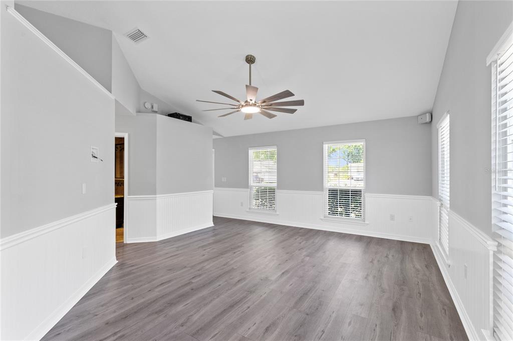 An empty room features gray wood-look flooring, white wainscoting, and a vaulted ceiling with a fan — 4103 BOB WHITE COURT, ST CLOUD, FL