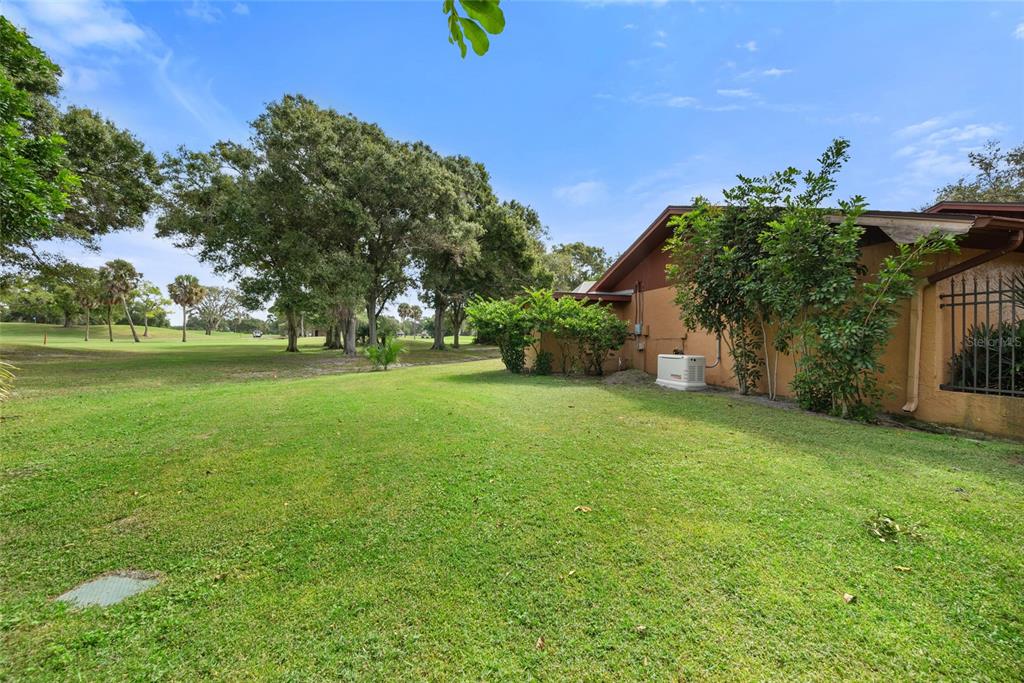 A grassy backyard view of a house exterior with a generator and golf course backdrop — 2674 CONCORDE COURT, CLEARWATER, FL