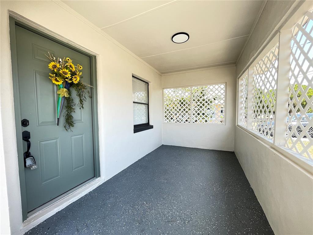A covered porch features a gray door with a wreath, white walls, and speckled flooring — 2015 6TH STREET NE, WINTER HAVEN, FL