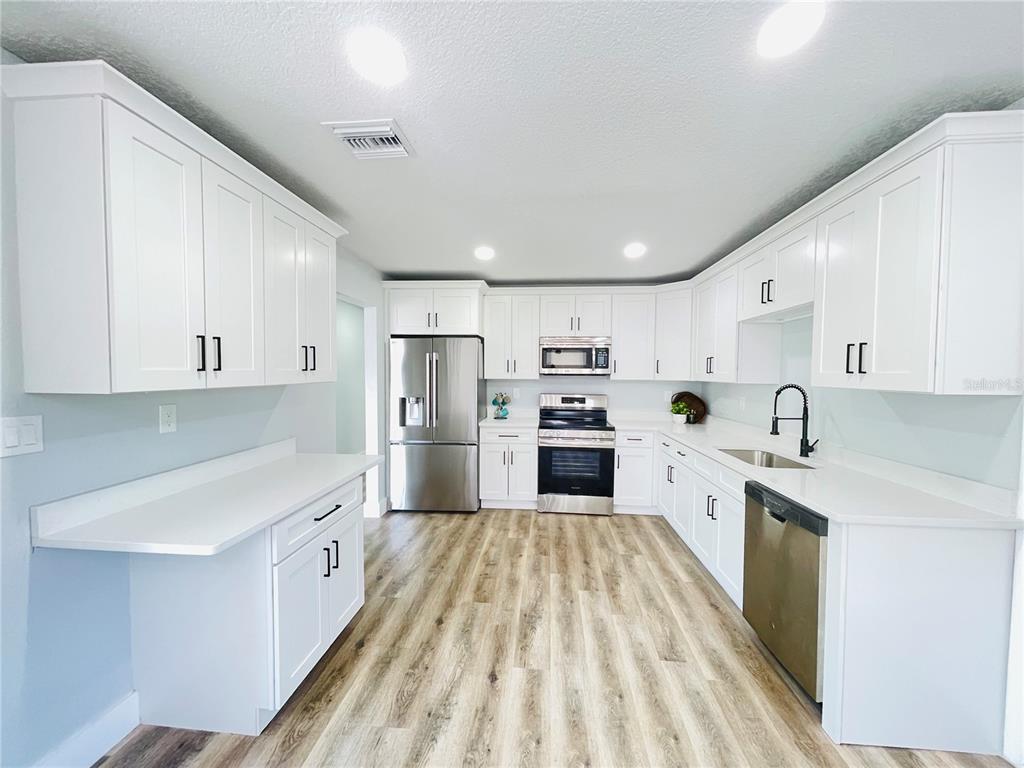 A kitchen features white cabinets, stainless steel appliances, quartz countertops, and light wood-look flooring — 2015 6TH STREET NE, WINTER HAVEN, FL
