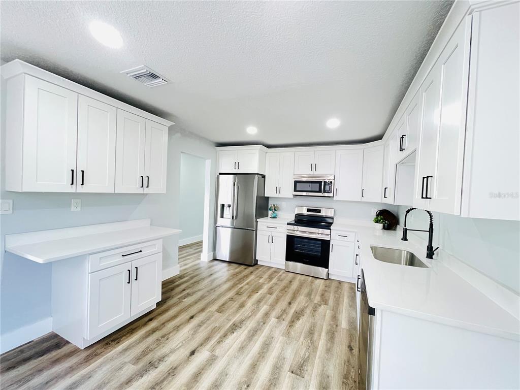 A modern kitchen features white cabinets, stainless steel appliances, and light wood-look flooring — 2015 6TH STREET NE, WINTER HAVEN, FL