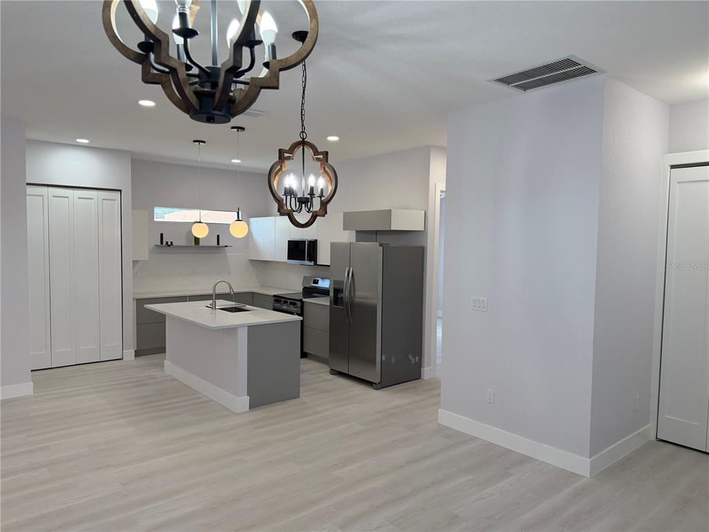A modern kitchen features gray lower cabinets, white upper cabinets, a central island, and stainless appliances — 3200 8TH STREET SW, LEHIGH ACRES, FL