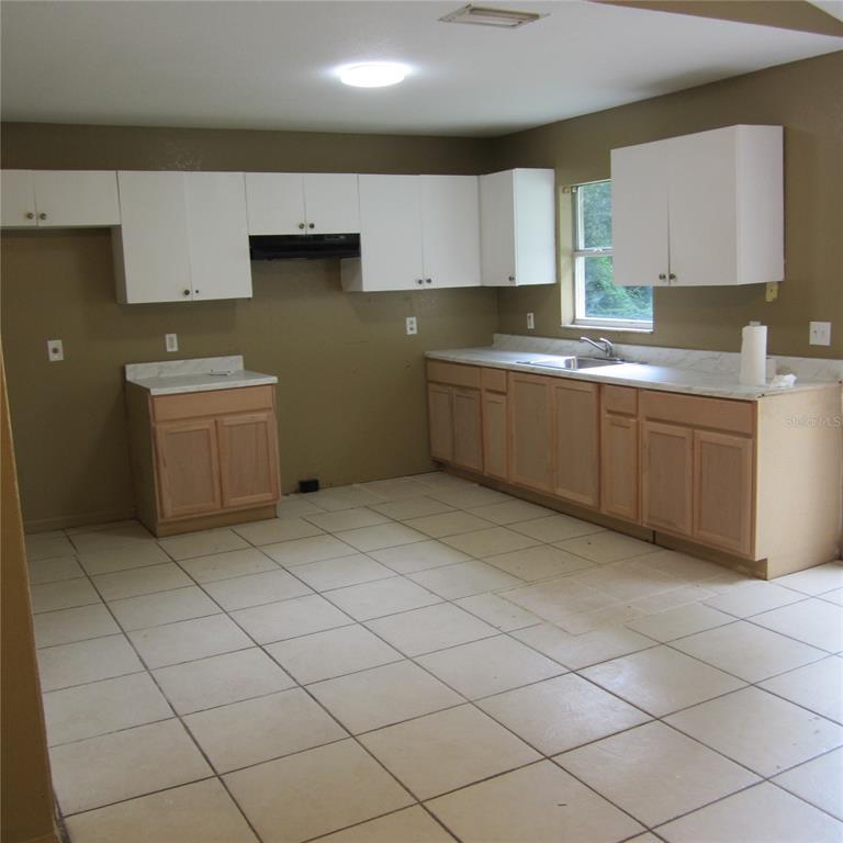A kitchen features white upper cabinets, light wood lower cabinets, and beige tile flooring — 1414 26TH STREET NW, WINTER HAVEN, FL