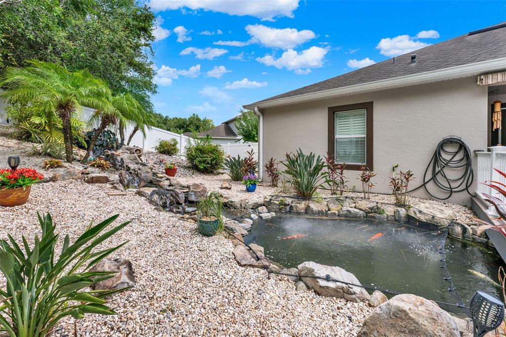 A backyard features a koi pond with a net, rock landscaping, and a house exterior — 1692 BLUE GRASS BOULEVARD, DELAND, FL