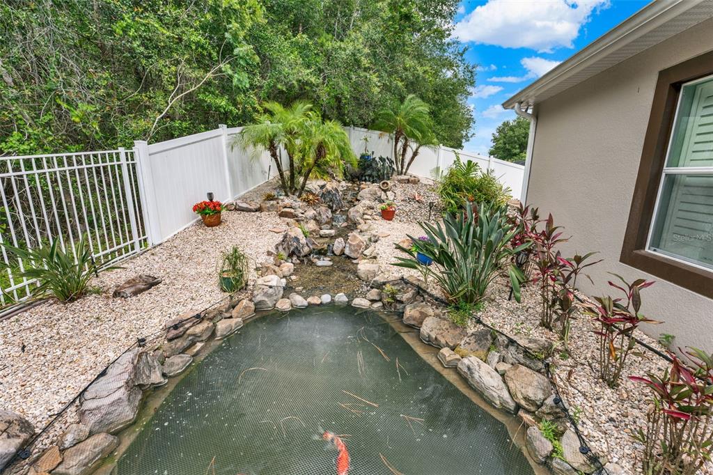 A backyard koi pond with a rock waterfall feature sits beside a house exterior — 1692 BLUE GRASS BOULEVARD, DELAND, FL