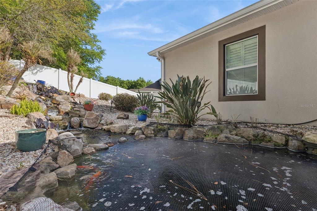 A backyard koi pond with a small waterfall sits beside a house with a window — 1692 BLUE GRASS BOULEVARD, DELAND, FL