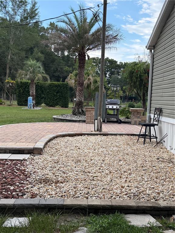 A backyard features a brick patio, a gravel area, a grill, and a palm tree — 2485 SE 174TH PLACE, SUMMERFIELD, FL