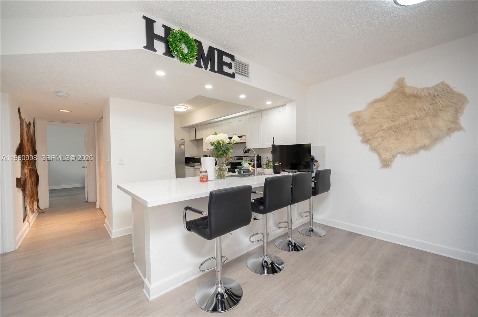 A kitchen features a white breakfast bar with four black stools and light flooring — 18890 NW 57 ave # 210, Hialeah FL 33015, HIALEAH, FL