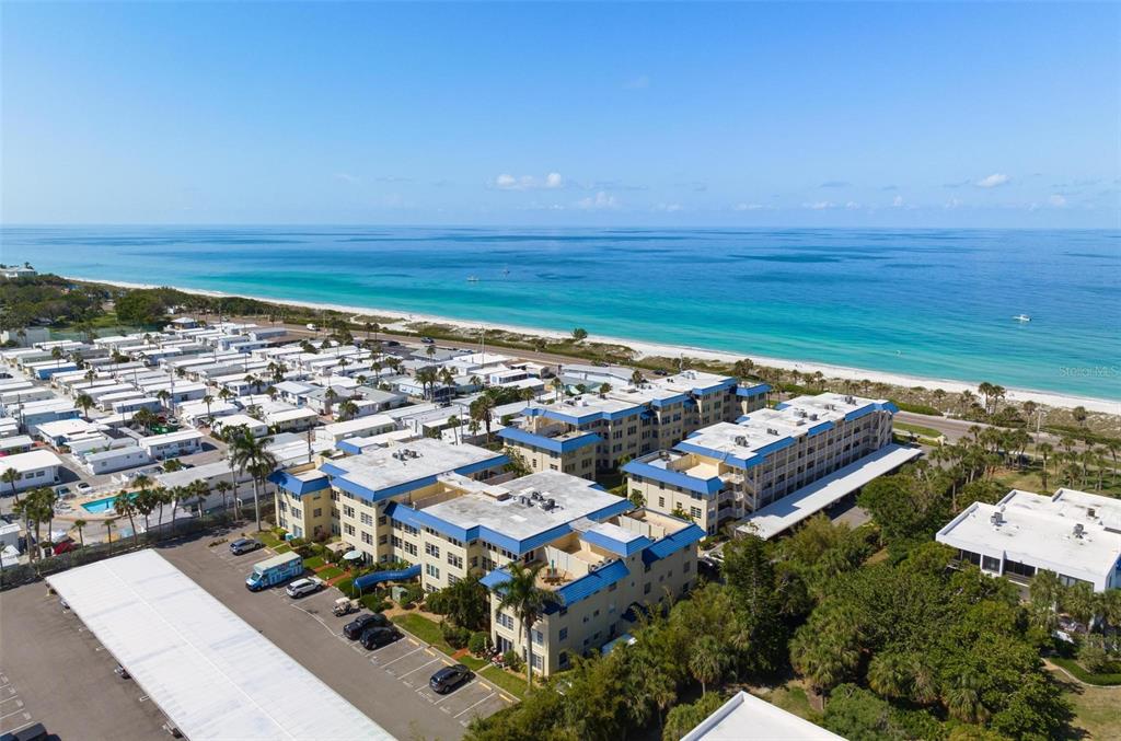 An aerial view shows a multi-story apartment complex located near a beach and ocean — 3806 GULF OF MEXICO DRIVE UNIT C202, LONGBOAT KEY, FL
