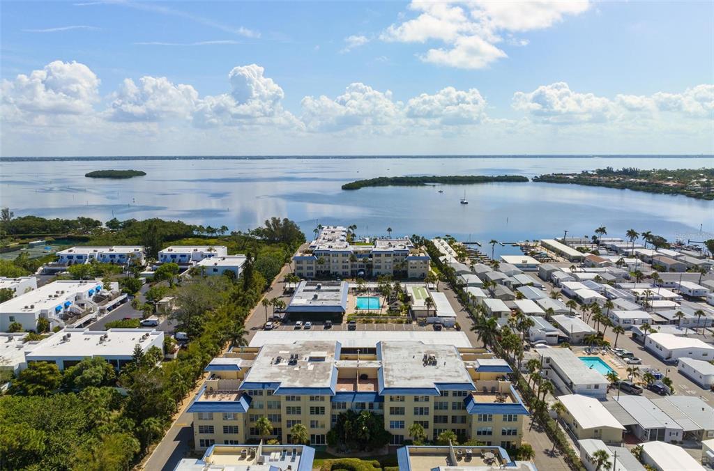 An aerial view shows a multi-story apartment complex near a large body of water — 3806 GULF OF MEXICO DRIVE UNIT C202, LONGBOAT KEY, FL
