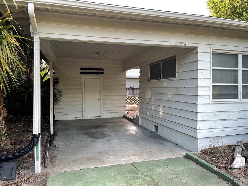 A white-sided house features a concrete carport with a small storage door and a window — 2415 PELICAN DRIVE, SARASOTA, FL