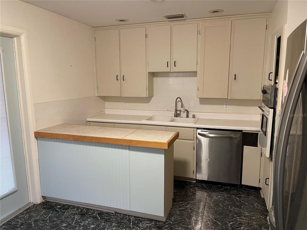 A kitchen features light-colored cabinets, a tiled peninsula countertop, and a stainless steel dishwasher — 2415 PELICAN DRIVE, SARASOTA, FL