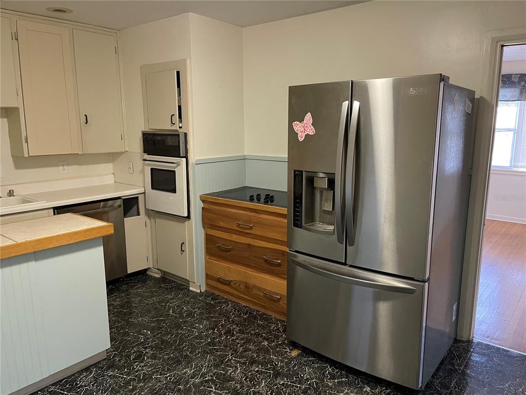 A kitchen features white cabinets, a stainless steel refrigerator, a built-in oven, and dark flooring — 2415 PELICAN DRIVE, SARASOTA, FL