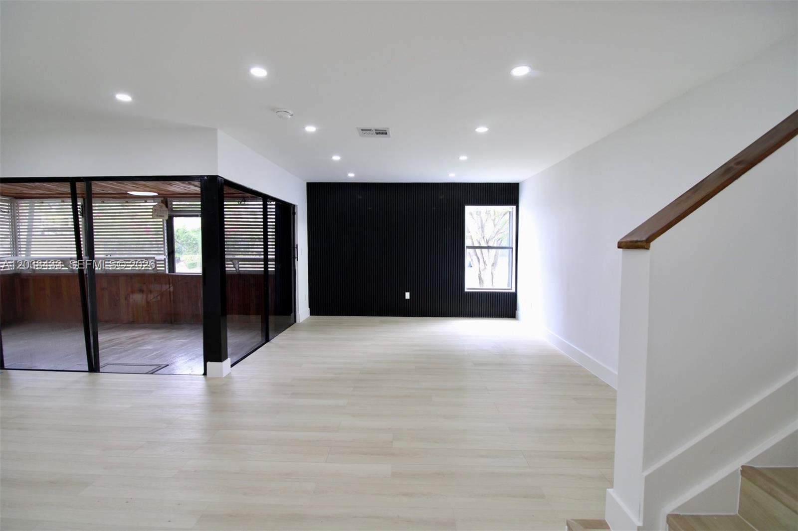 A bright room features light wood-look flooring, a black slatted accent wall, and a staircase — 21808 SW 99th Ave, Cutler Bay FL 33190, CUTLER BAY, FL