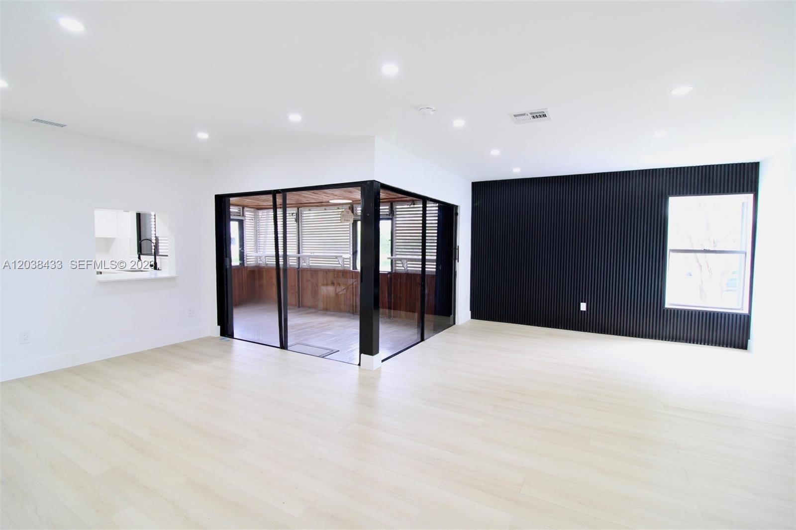 A bright room features light wood flooring, a black accent wall, and a glass-enclosed porch — 21808 SW 99th Ave, Cutler Bay FL 33190, CUTLER BAY, FL