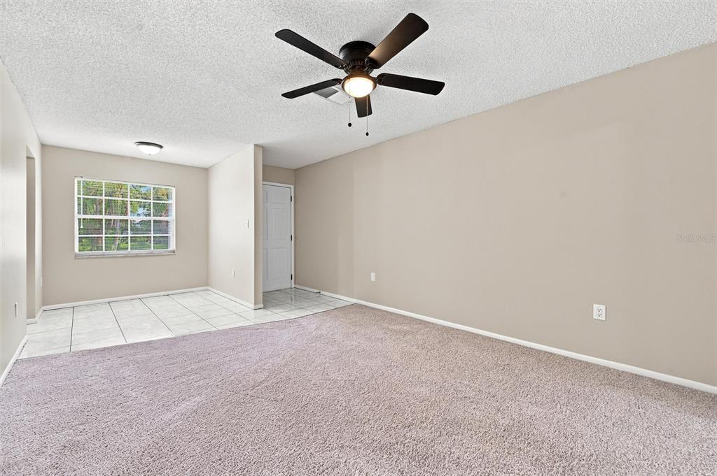 A room with carpeted flooring, a ceiling fan, and an adjacent tiled dining area — 4215 E BAY DRIVE UNIT 405, CLEARWATER, FL