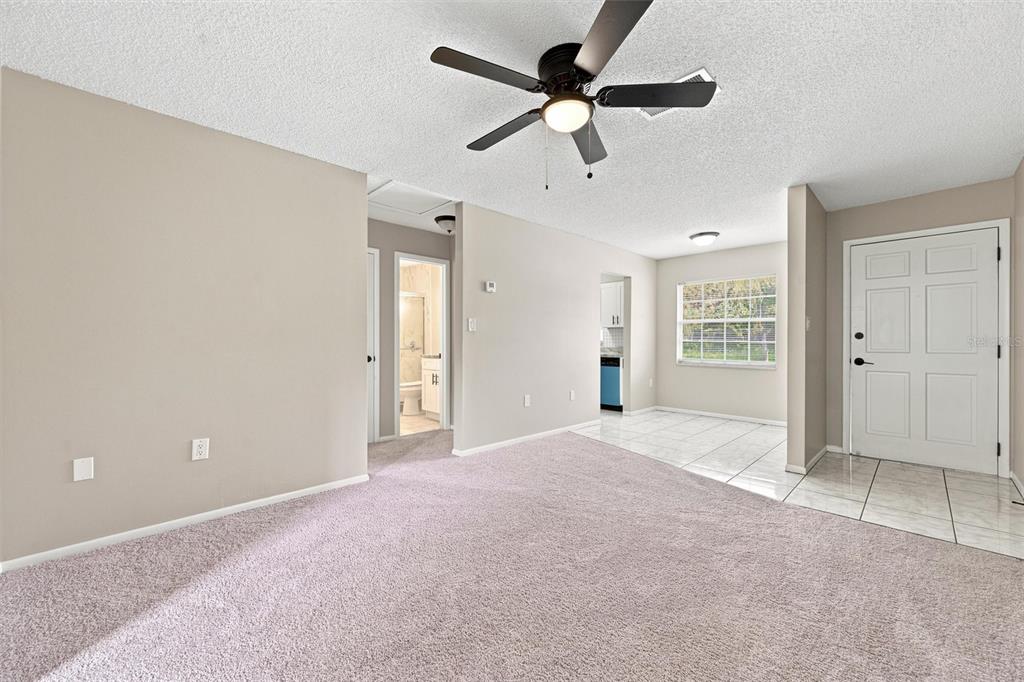 A living room with beige carpet, a ceiling fan, and an adjacent tiled entryway — 4215 E BAY DRIVE UNIT 405, CLEARWATER, FL