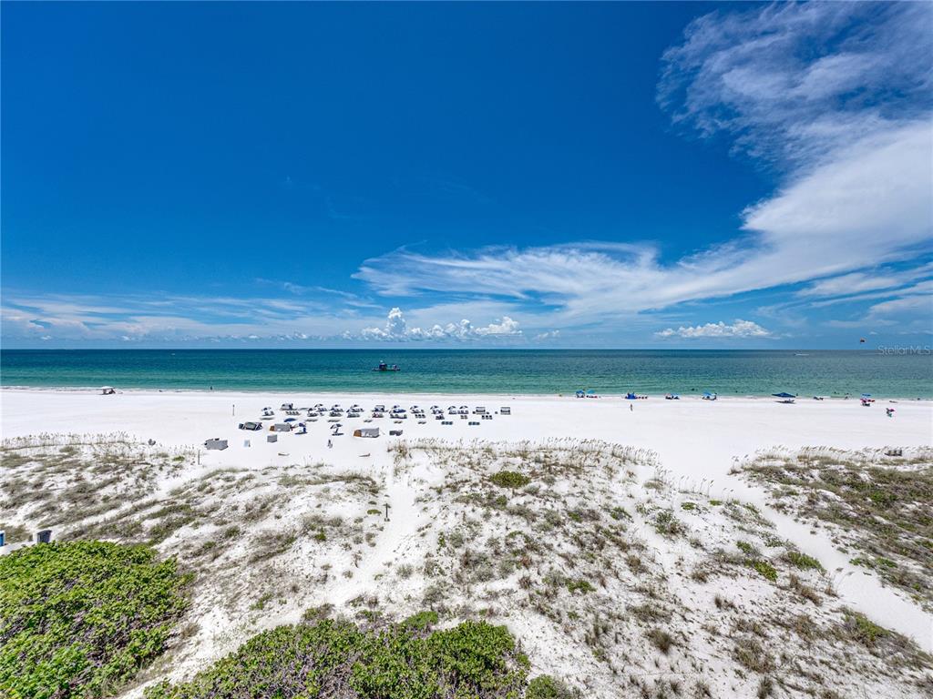 A wide, sandy beach with dunes and scattered umbrellas overlooks the ocean under a blue sky — 3910 GULF BOULEVARD UNIT 400, ST PETE BEACH, FL
