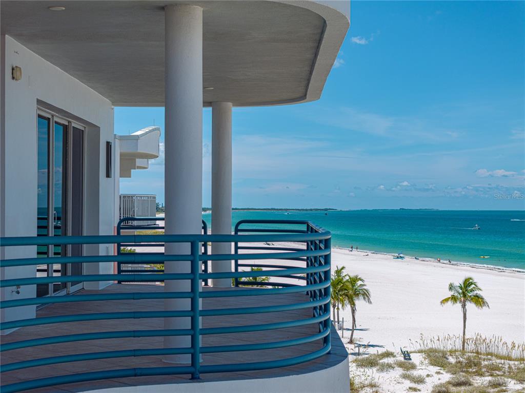 A balcony with blue railings overlooks a white sand beach and the ocean — 3910 GULF BOULEVARD UNIT 400, ST PETE BEACH, FL