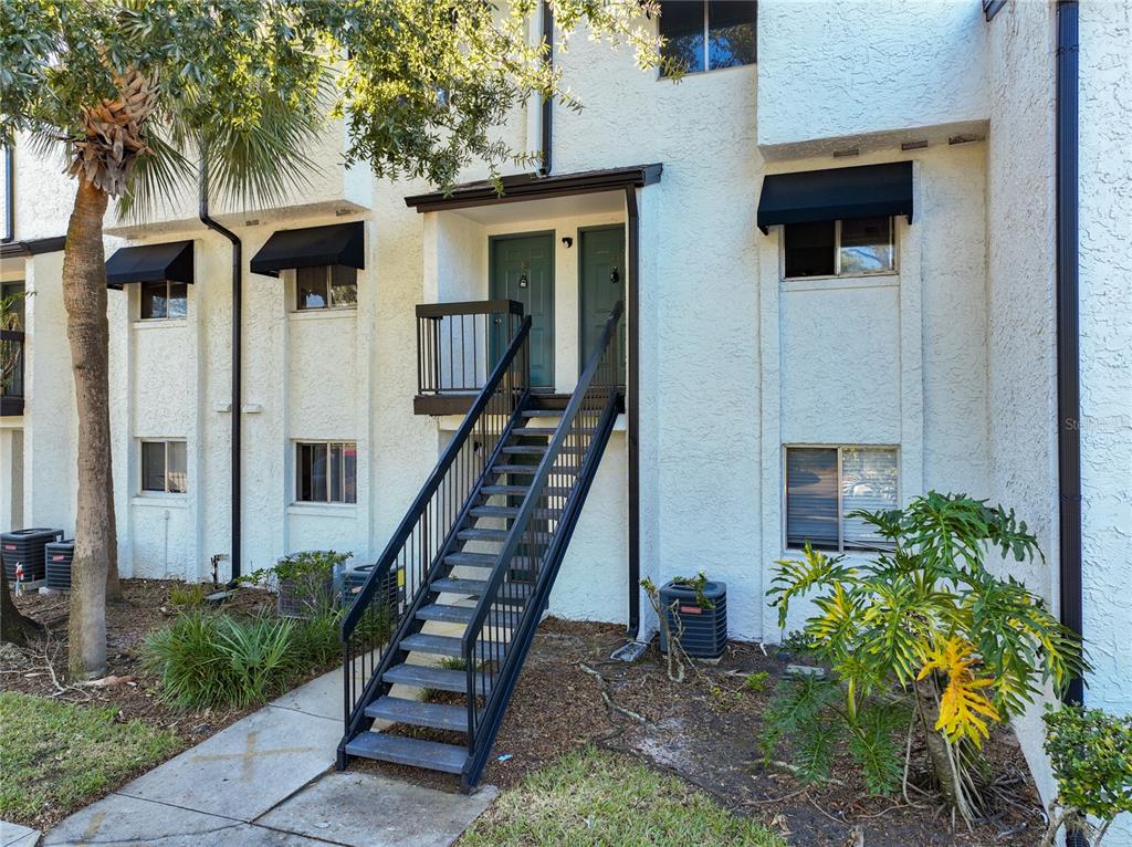 An exterior view of a two-story apartment building with a central staircase and teal doors — 4117 S SEMORAN BOULEVARD UNIT 14, ORLANDO, FL