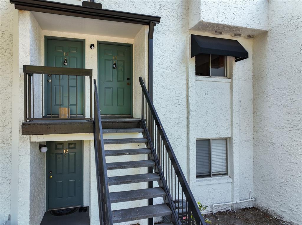 An exterior view of a two-story building with green doors, a staircase, and stucco walls — 4117 S SEMORAN BOULEVARD UNIT 14, ORLANDO, FL