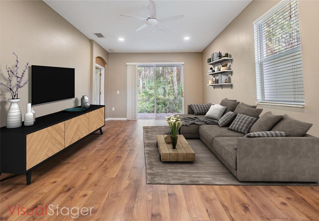 This is a digitally staged living room featuring wood-look flooring, a sectional sofa, and a television — 12441 CAVALIER COURT, HUDSON, FL