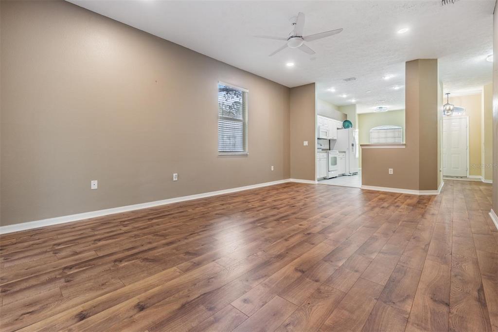 An open-concept living area features wood-look flooring, a ceiling fan, and an adjacent kitchen — 12441 CAVALIER COURT, HUDSON, FL
