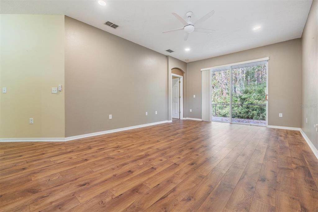 An empty living room features wood-look flooring, a ceiling fan, and sliding glass patio doors — 12441 CAVALIER COURT, HUDSON, FL