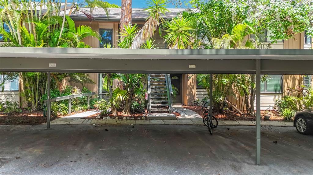 A covered parking area sits in front of a multi-story apartment building with lush landscaping — 1715 PELICAN COVE ROAD UNIT GL339, SARASOTA, FL