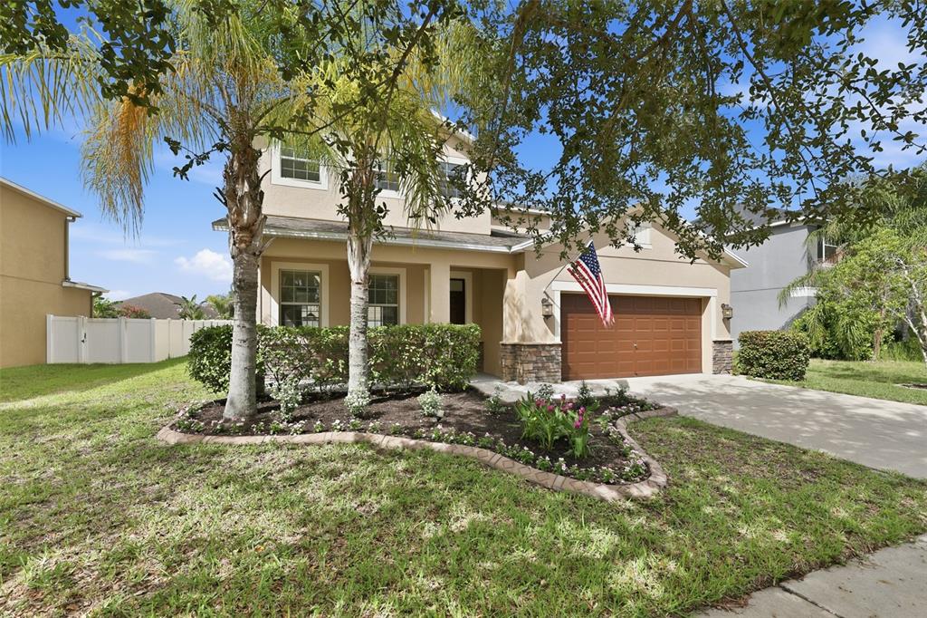 A two-story suburban house with a tan stucco exterior, a brown garage door, and landscaping — 10811 KIRKWALL PORT DRIVE, WIMAUMA, FL