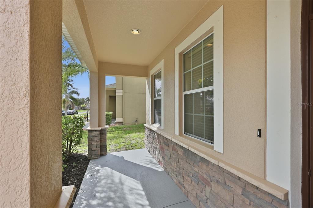 A covered front porch features a stone-accented wall, a window, and a concrete floor — 10811 KIRKWALL PORT DRIVE, WIMAUMA, FL