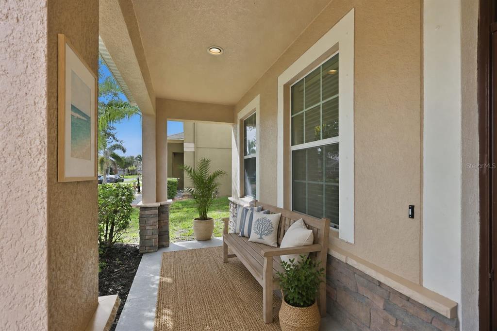 A covered front porch features a wooden bench, a woven rug, and stone accents — 10811 KIRKWALL PORT DRIVE, WIMAUMA, FL