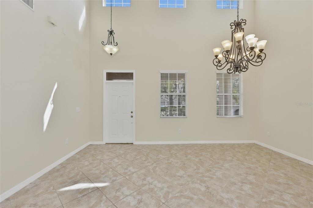 A high-ceilinged room with tile flooring, a chandelier, a front door, and two windows — 10811 KIRKWALL PORT DRIVE, WIMAUMA, FL
