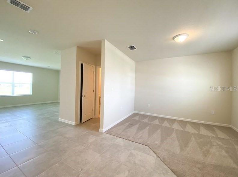 An interior view shows a room with beige carpet, tiled flooring, and a white door — 1579 ASPEN AVENUE, DAVENPORT, FL
