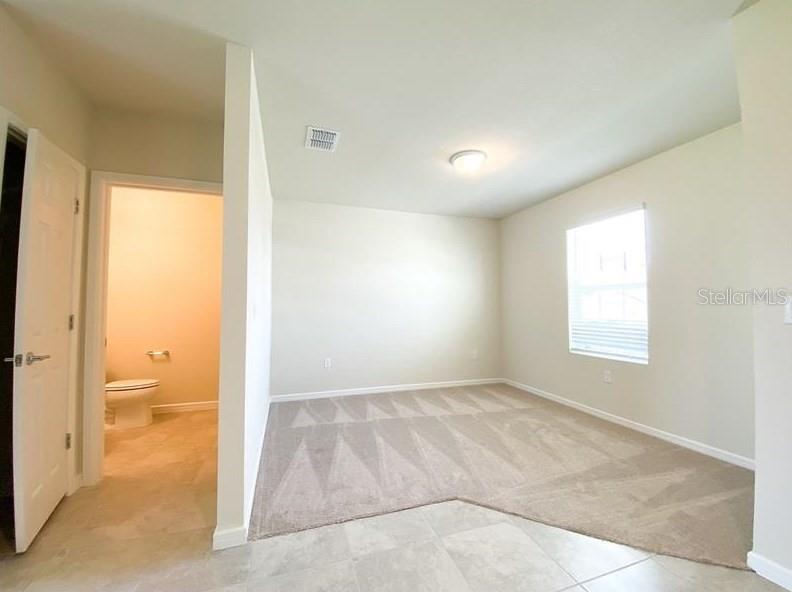 A room with beige carpet and tile flooring features an open doorway to a bathroom — 1579 ASPEN AVENUE, DAVENPORT, FL