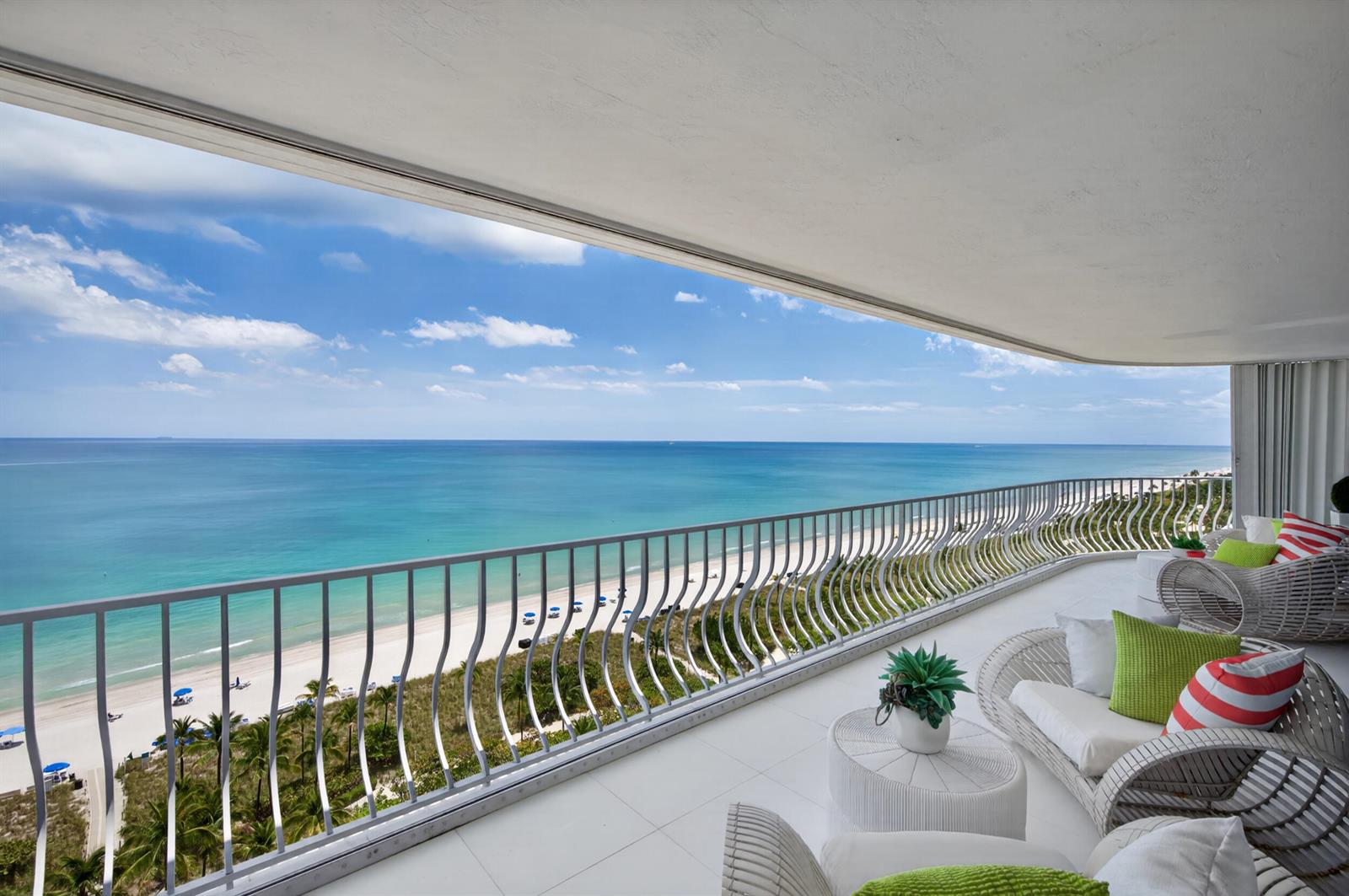 A balcony with white wicker furniture overlooks a sandy beach and the blue ocean — 10155 Collins Avenue # 1401, Bal Harbour FL 33154, BAL HARBOUR, FL