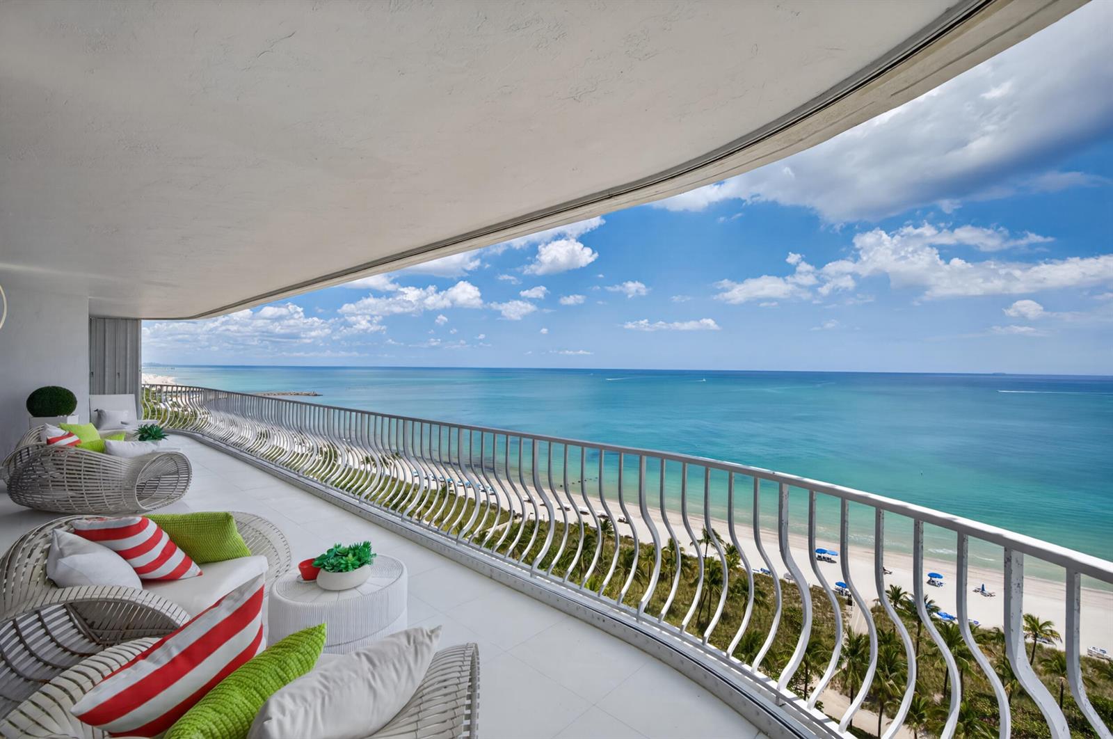 A curved balcony with white wicker furniture overlooks a sandy beach and the ocean — 10155 Collins Avenue # 1401, Bal Harbour FL 33154, BAL HARBOUR, FL