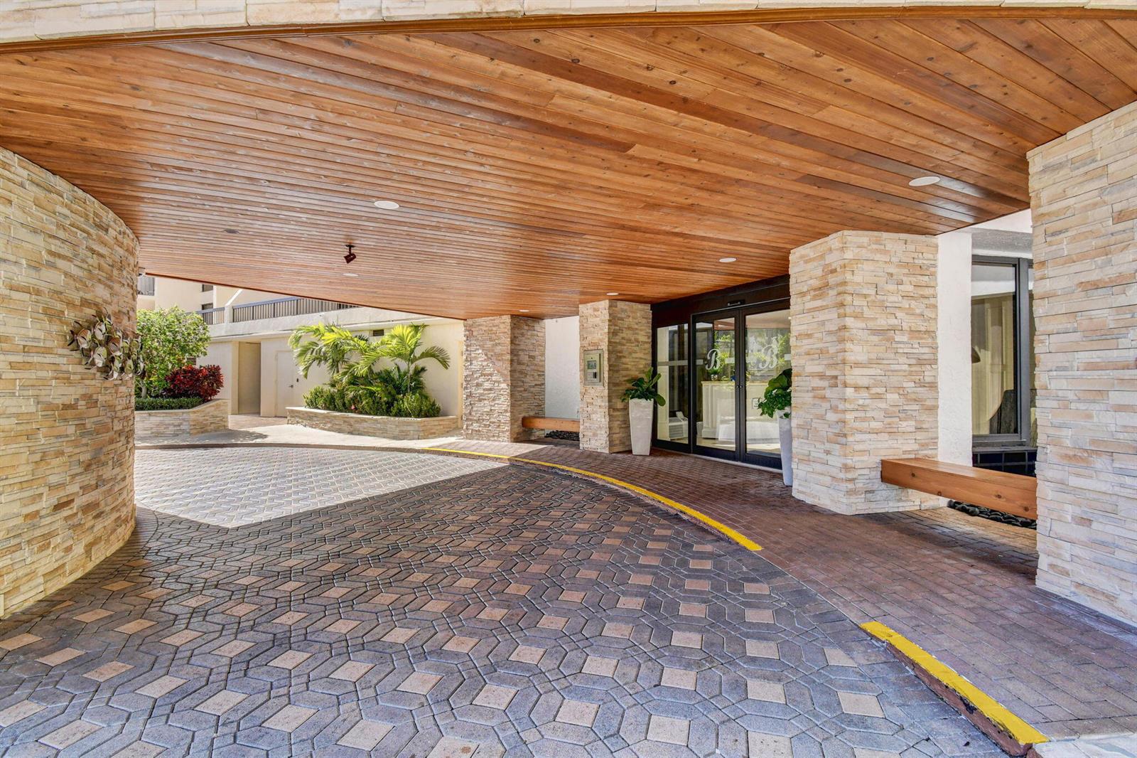A covered entrance features a wood-paneled ceiling, stone pillars, and a patterned brick driveway — 4740 S Ocean Boulevard # 1503, Boca Raton FL 33487, BOCA RATON, FL