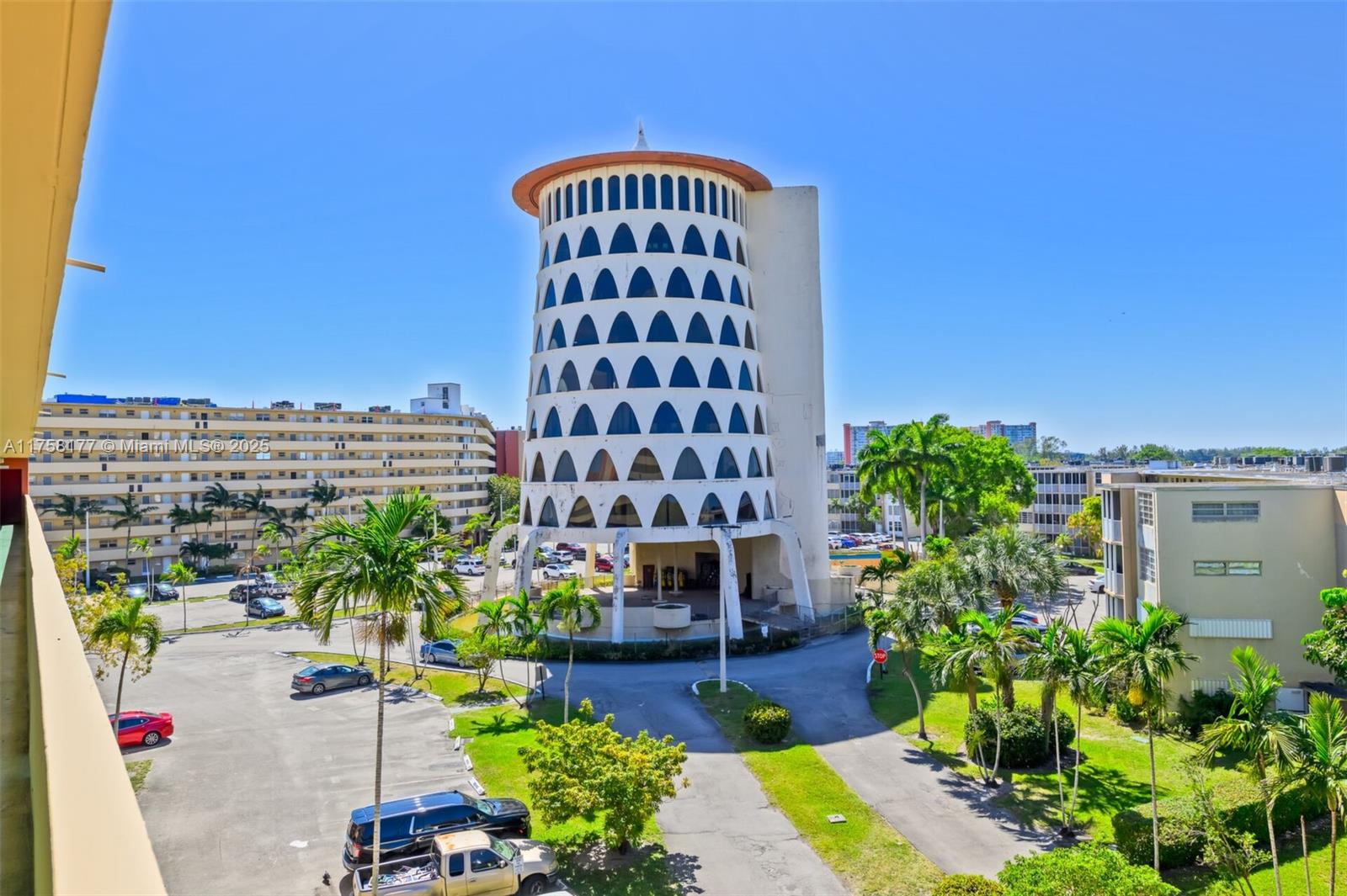 An exterior view shows a distinctive cylindrical apartment building with arched windows surrounded by palm trees — 1770 NE 191st St # 1, Miami FL 33179, MIAMI, FL
