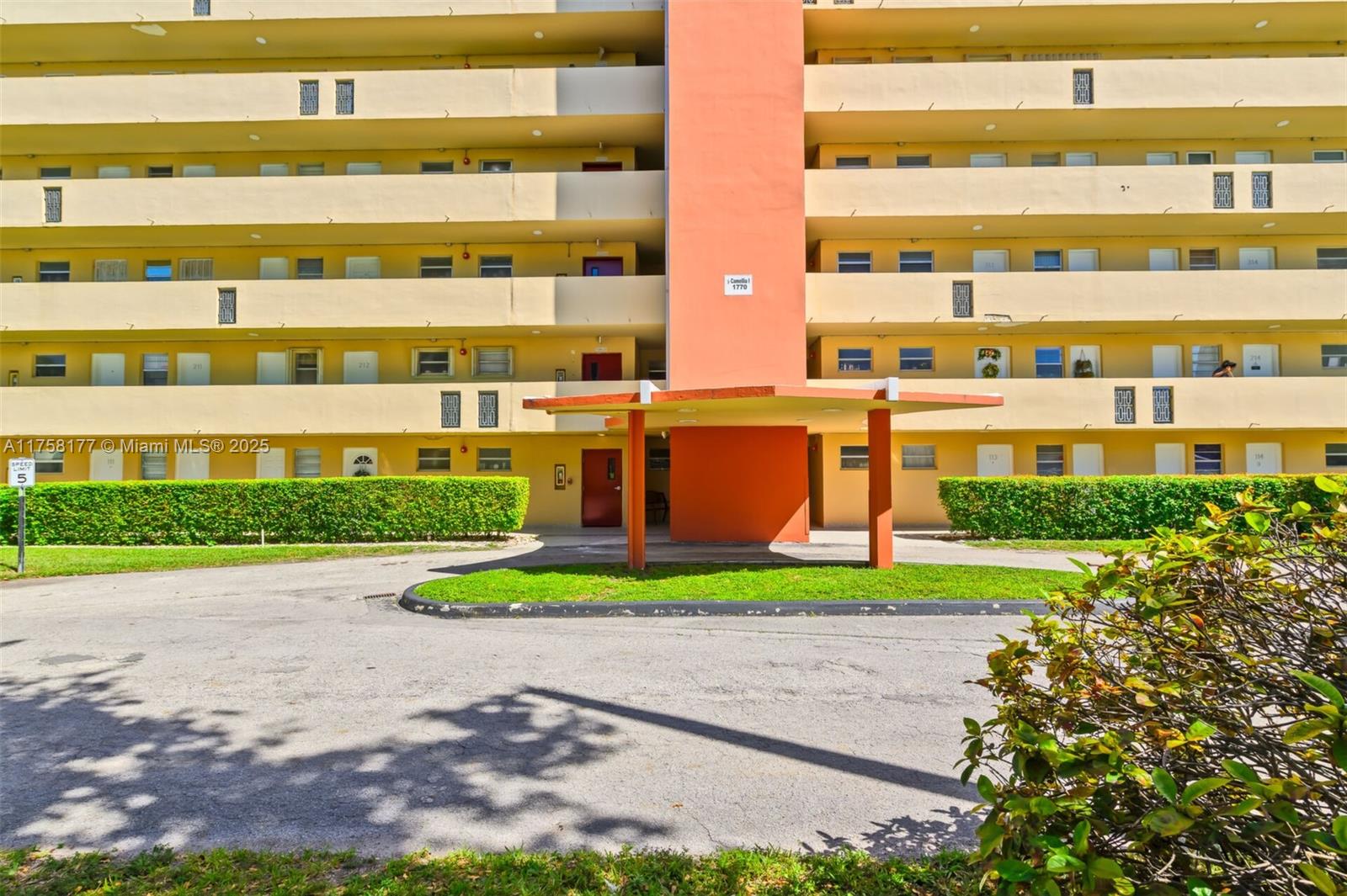 The exterior of a multi-story yellow apartment building features a central orange entrance canopy — 1770 NE 191st St # 1, Miami FL 33179, MIAMI, FL