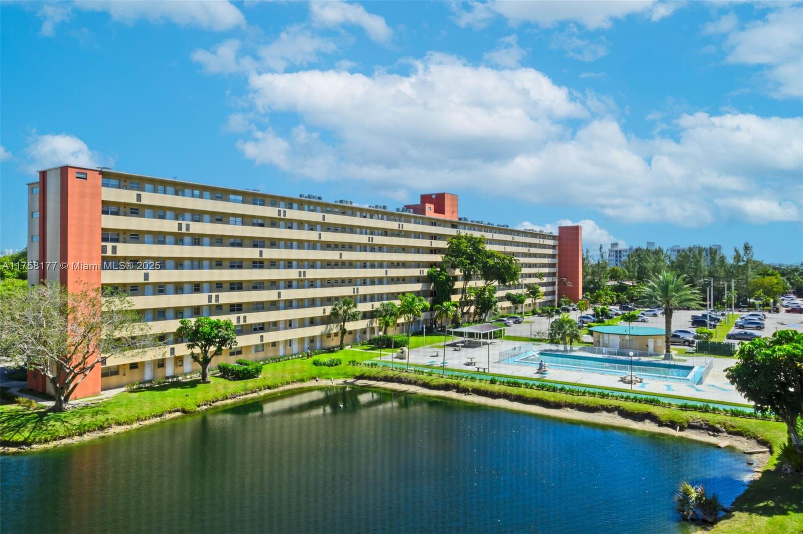 An exterior view of a multi-story apartment building with a pool and a pond — 1770 NE 191st St # 1, Miami FL 33179, MIAMI, FL