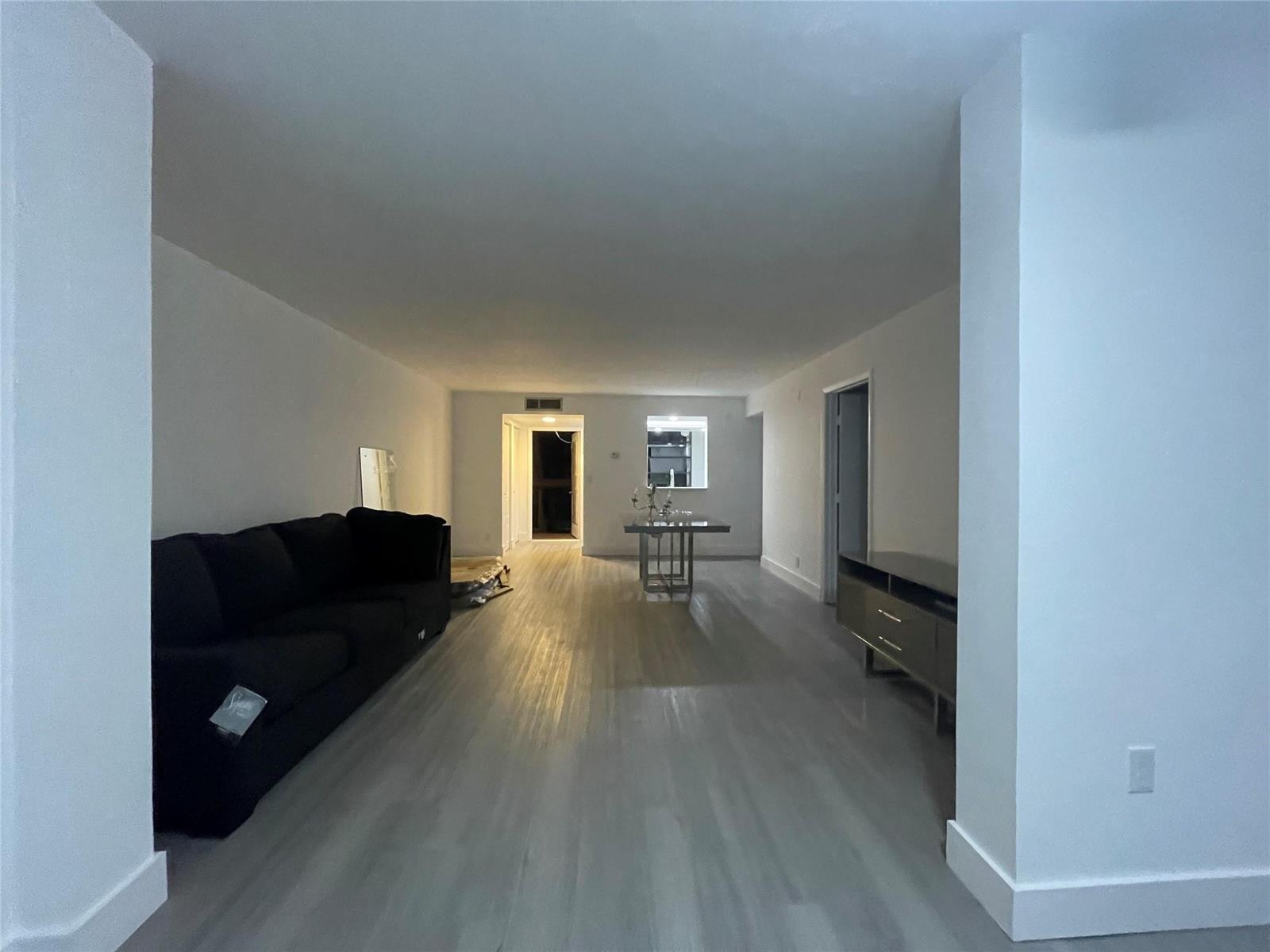 A long, open-concept living area features light wood-look flooring, white walls, and a black sofa — 7460 NW 18th Street # 201, Margate FL 33063, MARGATE, FL