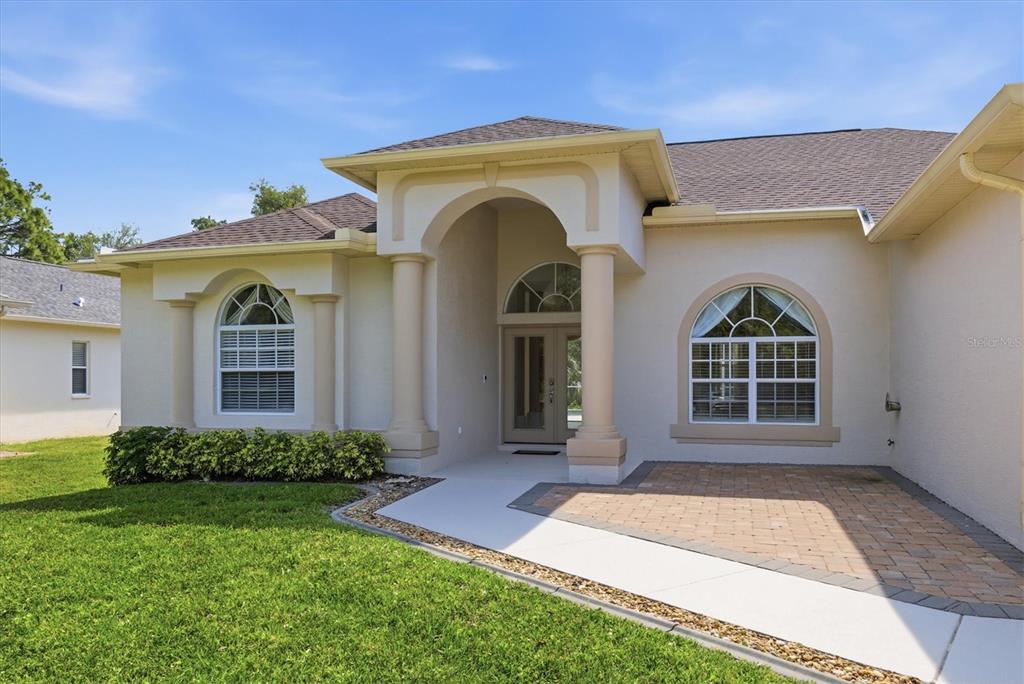 A single-story house with a beige stucco exterior, arched windows, and a paved front walkway — 2635 MANASOTA BEACH ROAD, ENGLEWOOD, FL