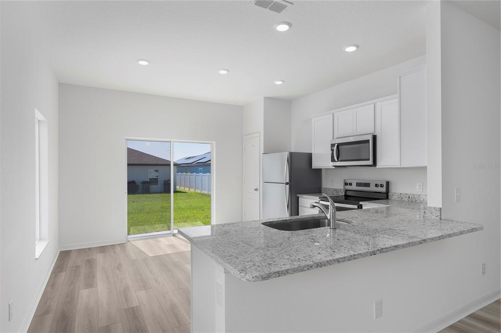 A kitchen with white cabinets, granite countertops, and a sliding glass door to the backyard — 3613 AMANATSU AVENUE, LAKE ALFRED, FL