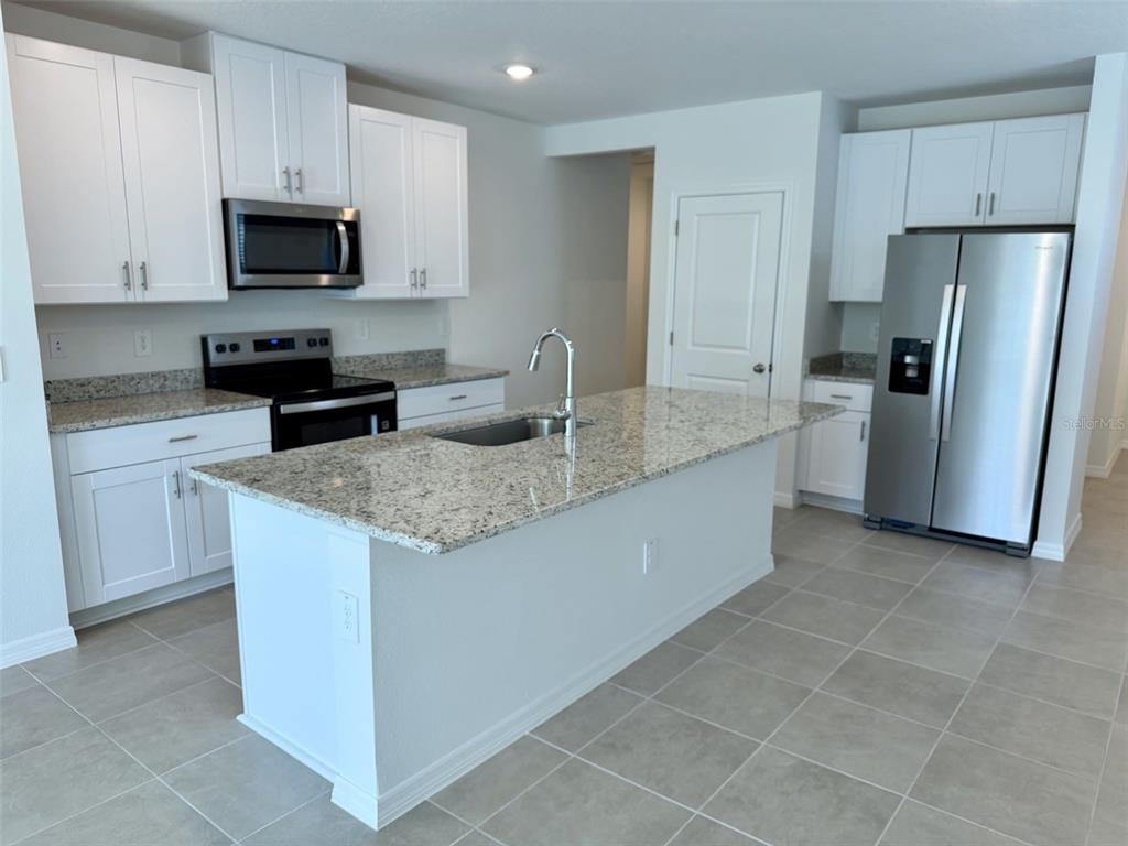 A kitchen features white cabinets, granite countertops, a center island with a sink, and appliances — 1483 BREKEY WAY, ZEPHYRHILLS, FL