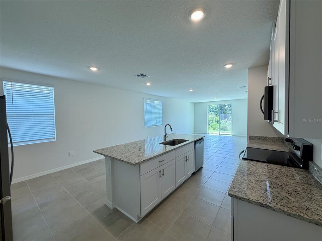A kitchen with white cabinets, granite countertops, a center island, and tile flooring — 1483 BREKEY WAY, ZEPHYRHILLS, FL