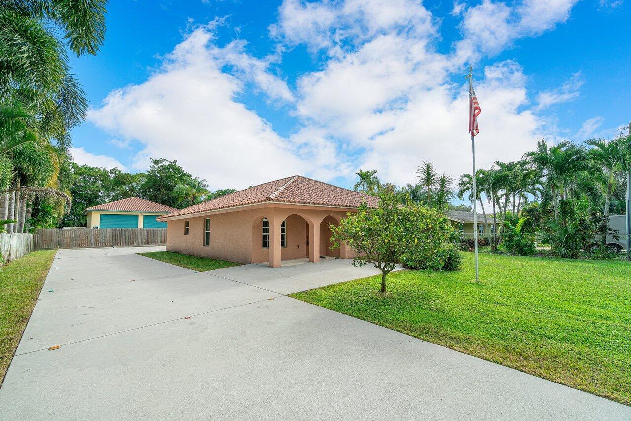 A single-story tan house with a tiled roof, a concrete driveway, and a flag pole — 5592 1st Road, Lake Worth FL 33467, LAKE WORTH, FL