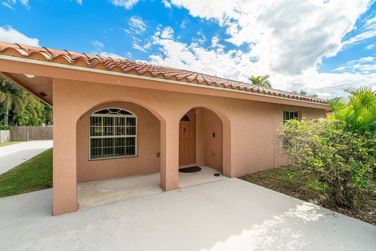 A peach-colored house exterior features a covered entryway with arched openings and a tiled roof — 5592 1st Road, Lake Worth FL 33467, LAKE WORTH, FL