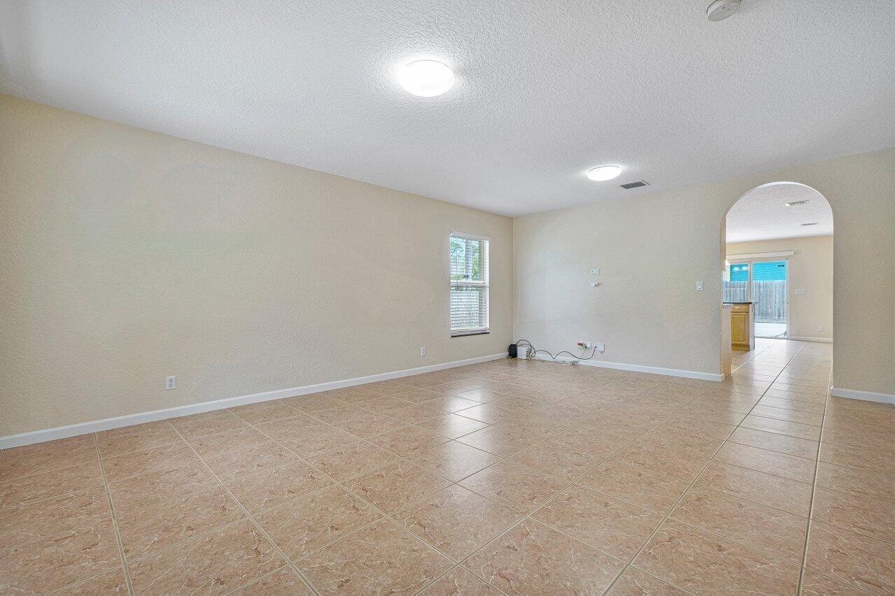 An empty living room with beige walls, tile flooring, and an arched doorway to the kitchen — 5592 1st Road, Lake Worth FL 33467, LAKE WORTH, FL